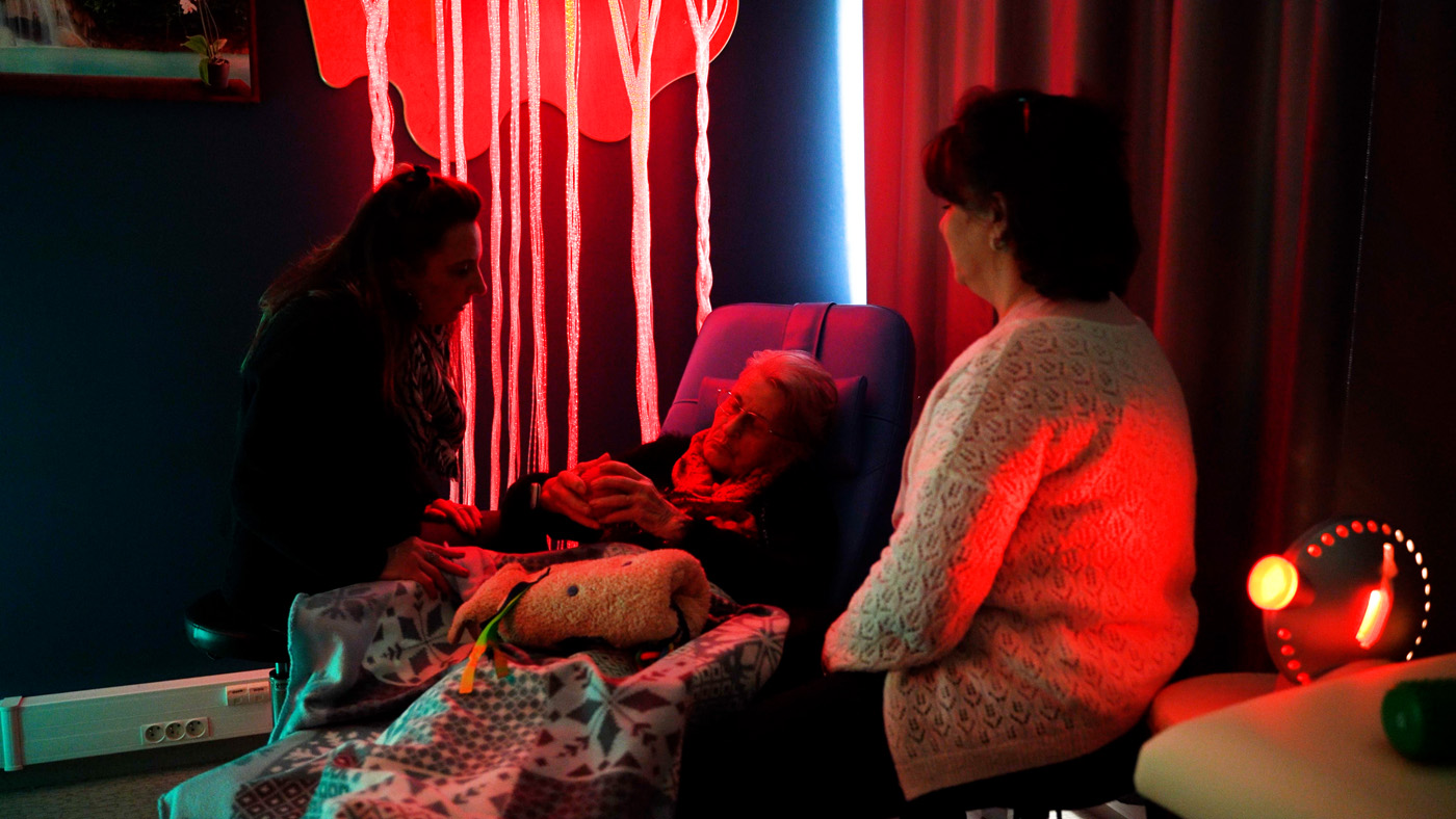 Caregivers assisting elderly woman in red-lit room
